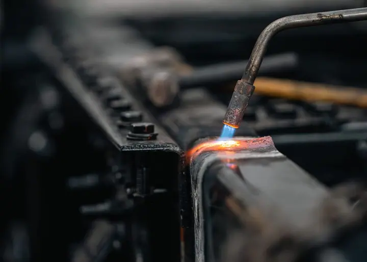 Close-up of a torch cutting a structural steel beam, sparks and blue flame