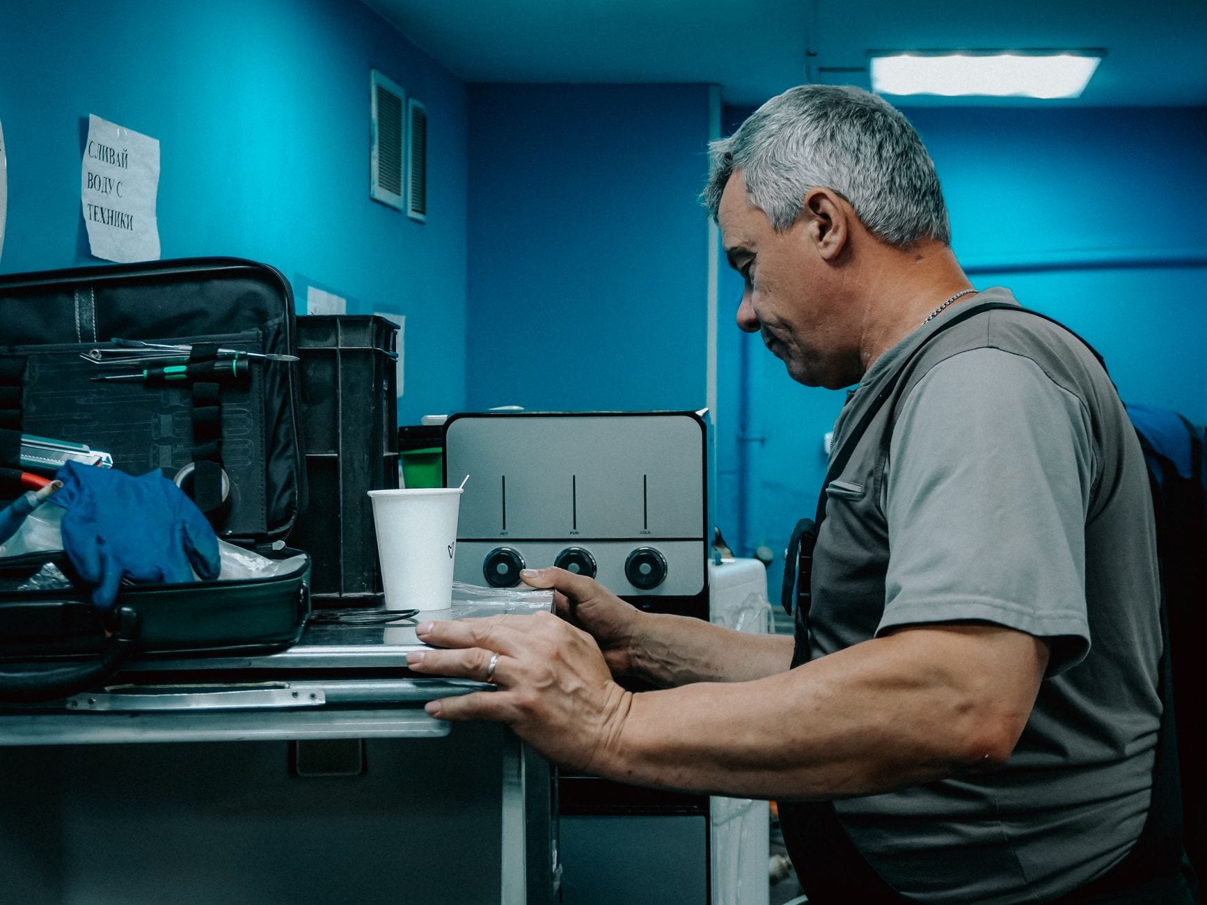 A male technician works on a machine in an industrial environment, focused on adjusting controls.