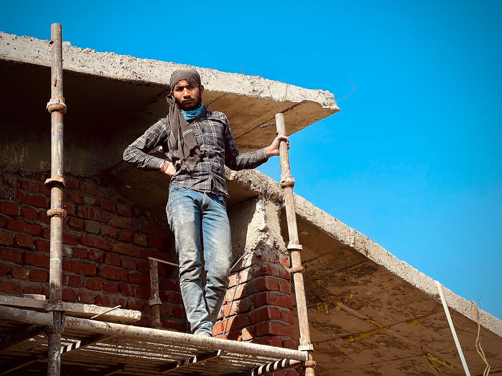 Worker standing on scaffolding in Rasulpur, India, posing confidently under clear skies.