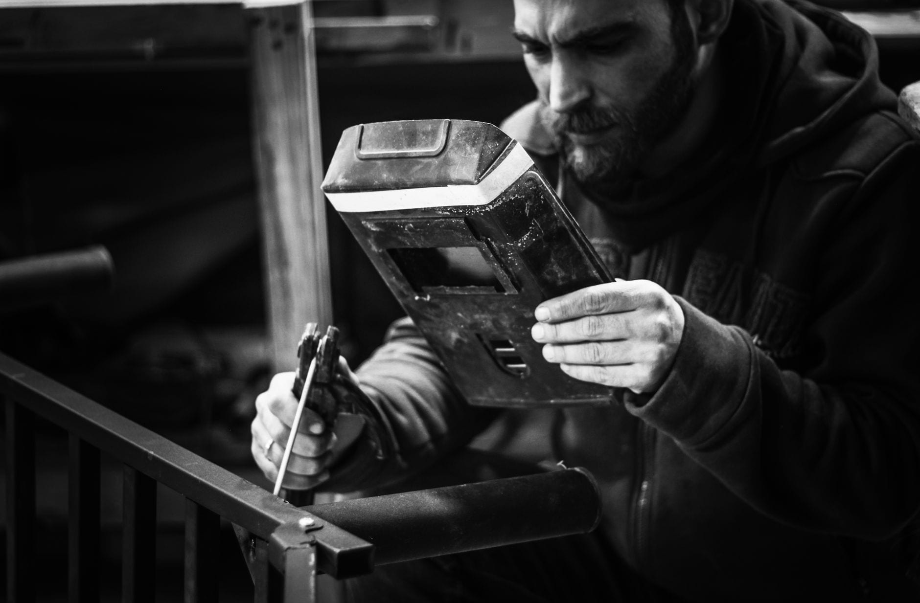 A black-and-white image of a welder inspecting his work with attention to detail.